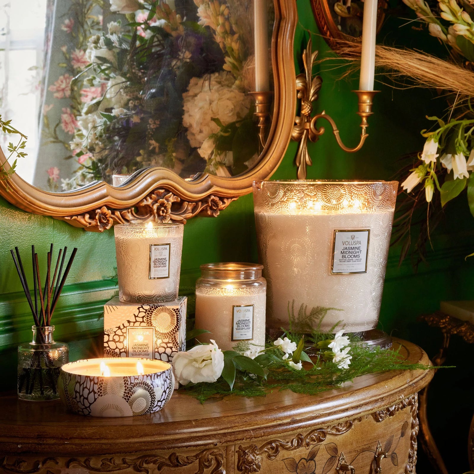 Decorative table setting with Jasmine Midnight Blooms candles, white flowers, and an antique mirror in the background.