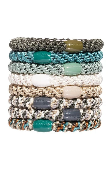 A stack of eight braided cord bracelets with smooth oval beads in various colors, including teal, sage green, white, beige, gray, and brown, set against a plain white background.