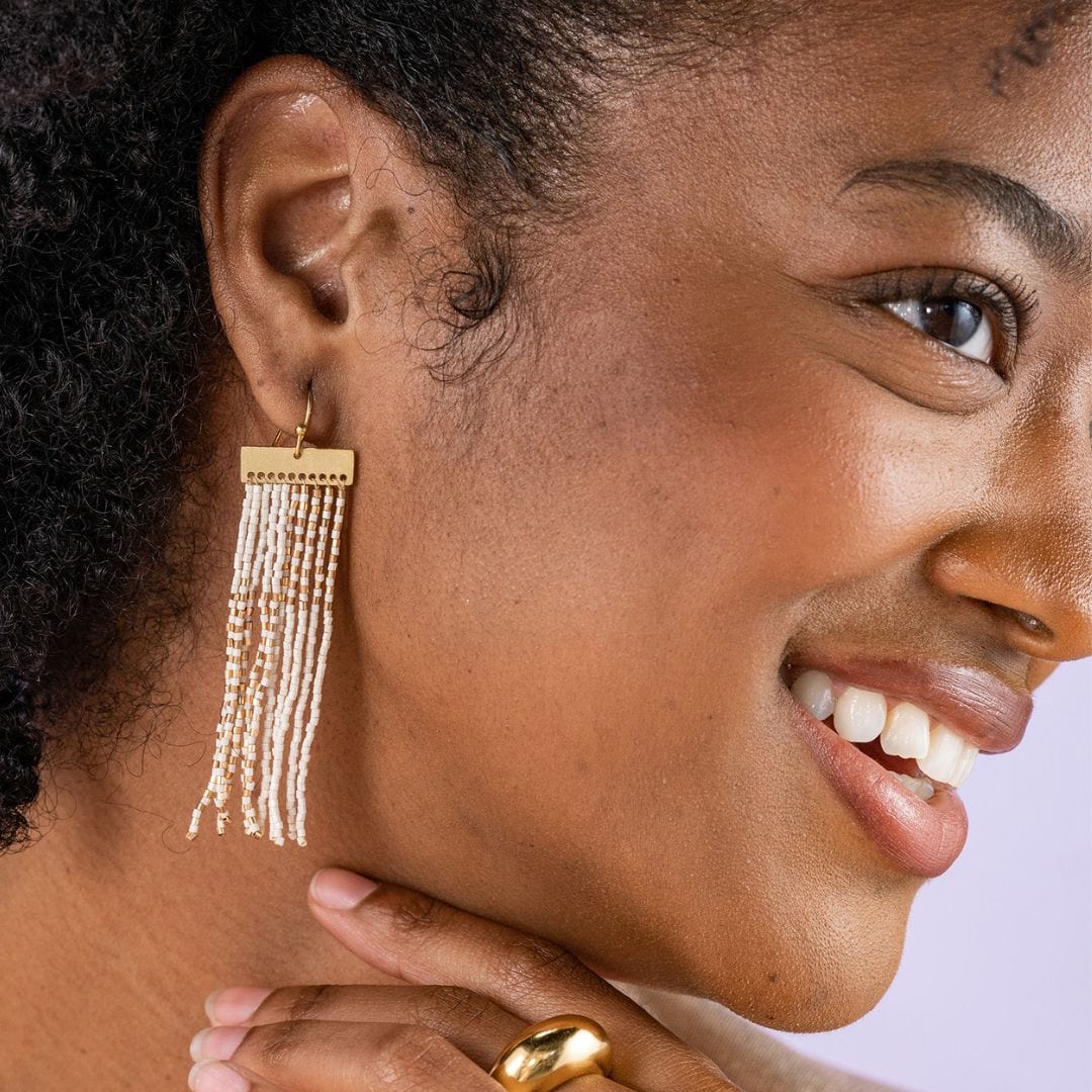 model wearing rectangle brass bar beaded fringe earrings in ivory & gold. 