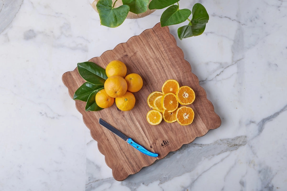 Hand made acacia wood cutting board with scalloped edge detailing displayed with luscious lemons. 