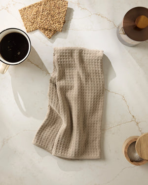 Latte colored waffle-textured towel on a marble surface with a cup of coffee and wooden items. Geometry towels. 