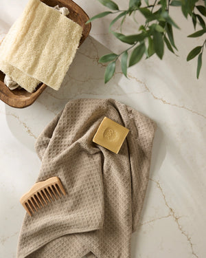 beige hand towel with a bar of soap, wooden comb, and plant on a marble surface. 
