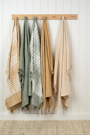 Four patterned cotton blankets hanging on a wooden rod against a white paneled wall.