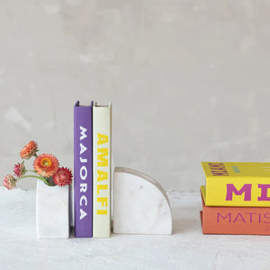 Marble vase bookend holding flowers and books with colorful titles on a light surface.