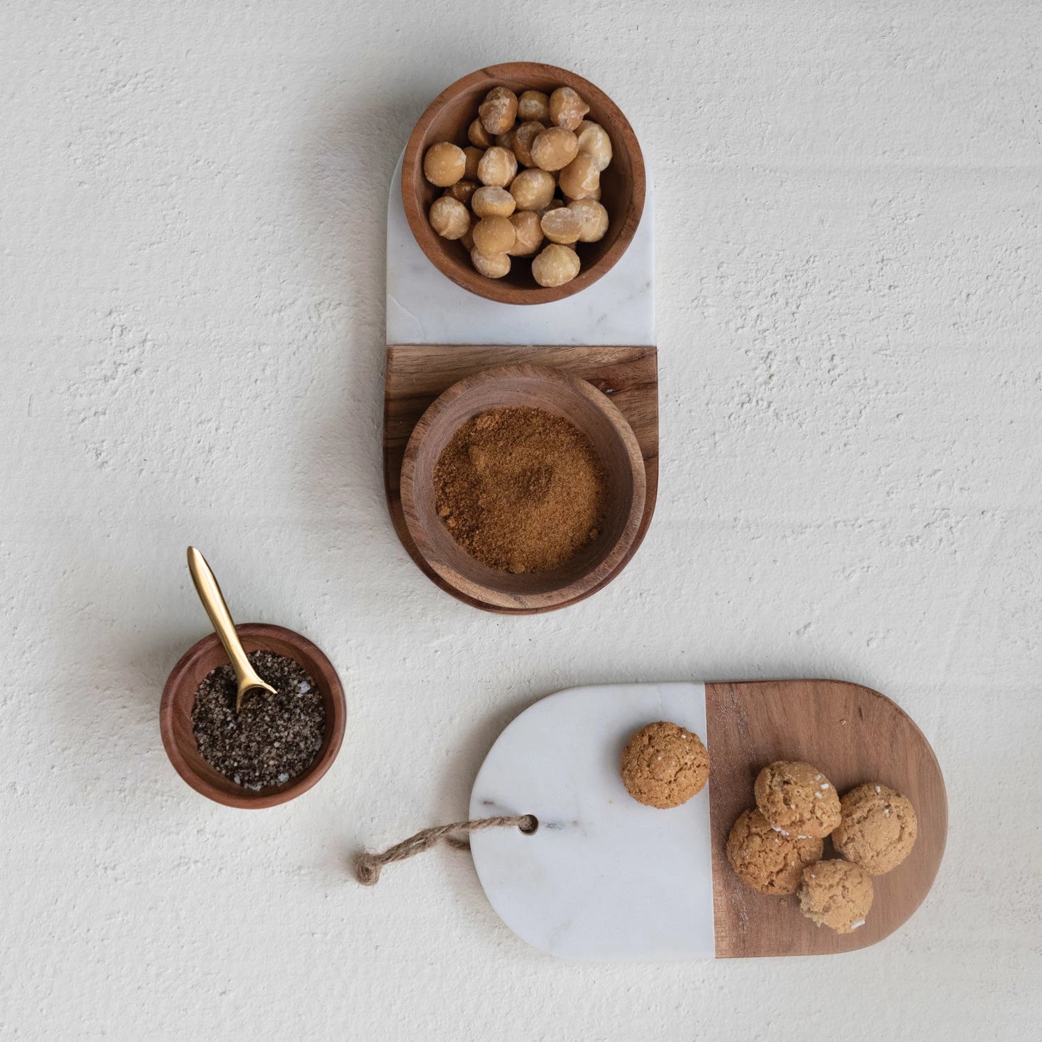 Array of white marble and acacia wood kitchen trays and pinch pots with spices. 