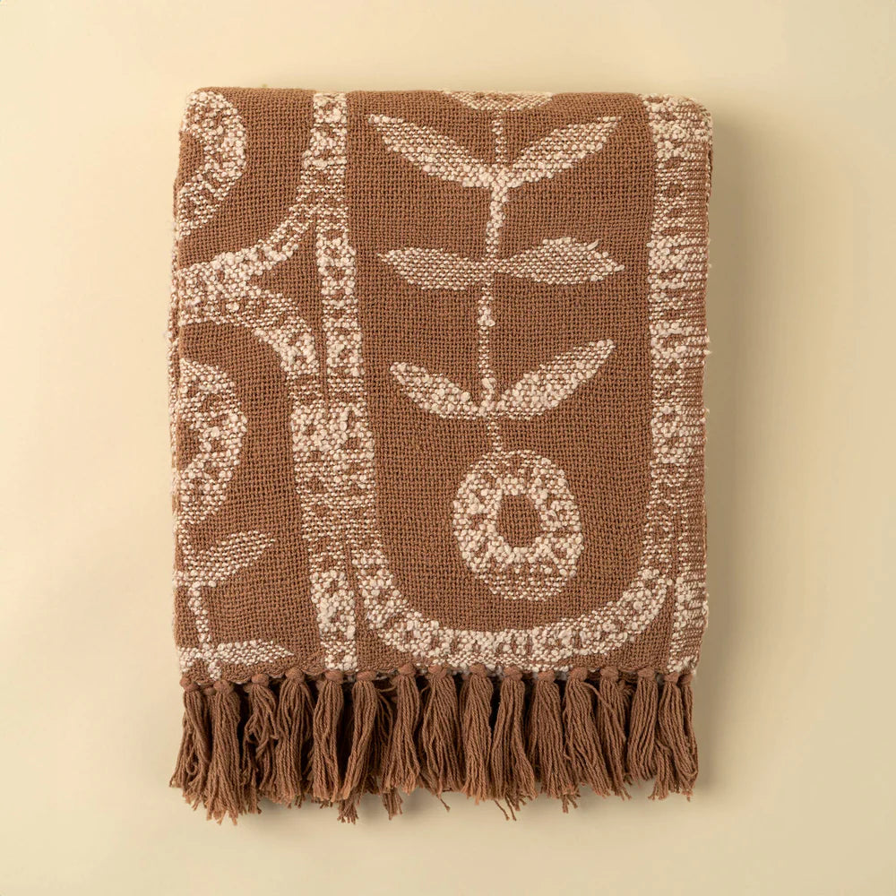 Brown and beige floral patterned cotton throw blanket, fringe edge detail on a beige background. 
