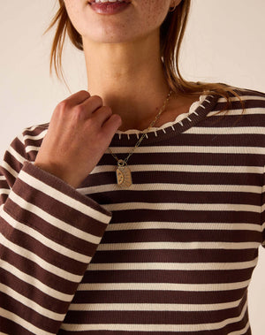 A close-up of a woman wearing a brown and cream striped knit top and a gold pendant necklace with a sun design.