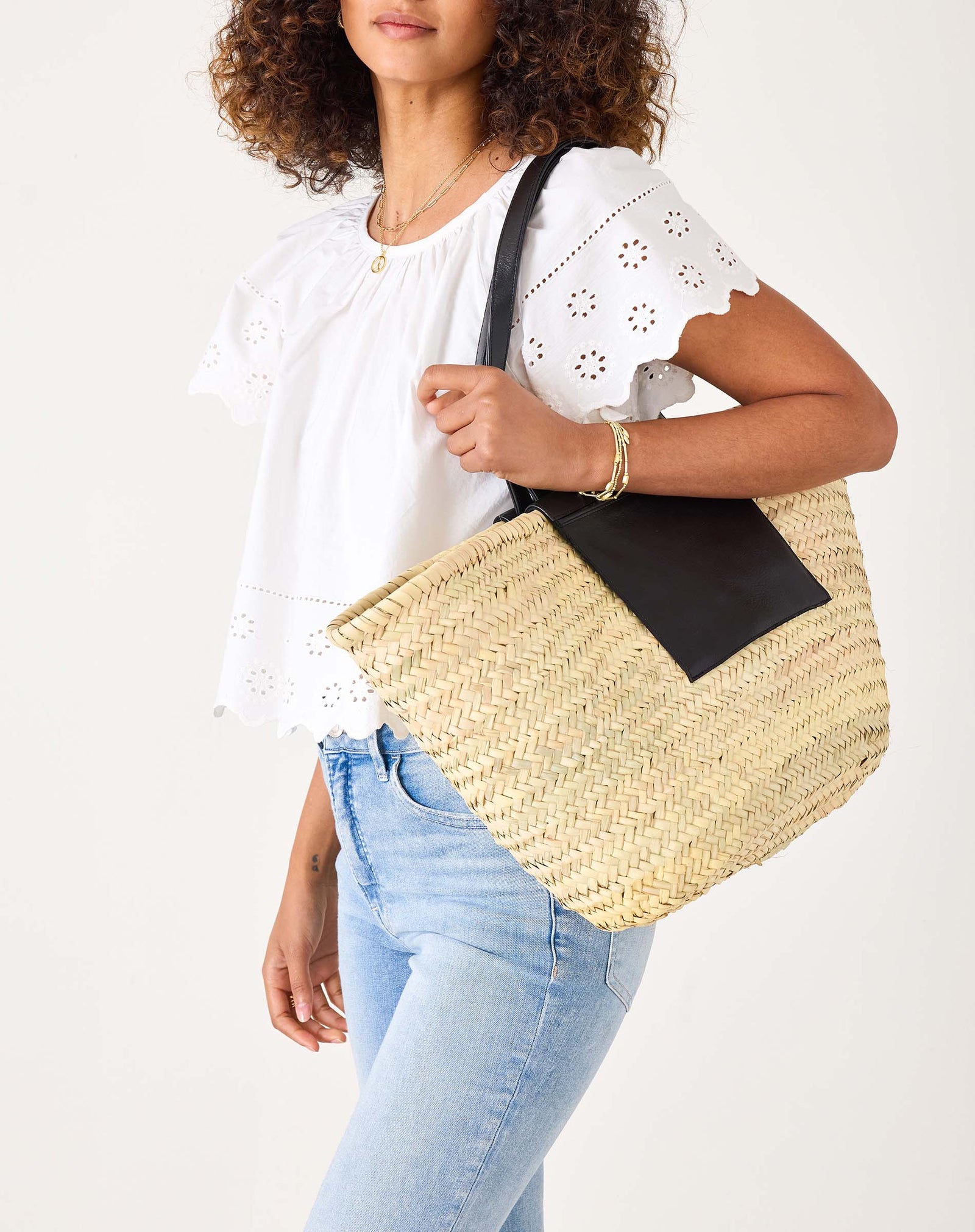 Woman holding a natural colored straw bag black leather pockets and handle against a plain background. Mersea. 