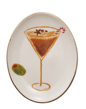 An oval white ceramic serving platter with a gold rim, featuring a hand-painted illustration of a martini glass with an orange-brown drink, a star anise garnish, a candy cane, and a green olivette.