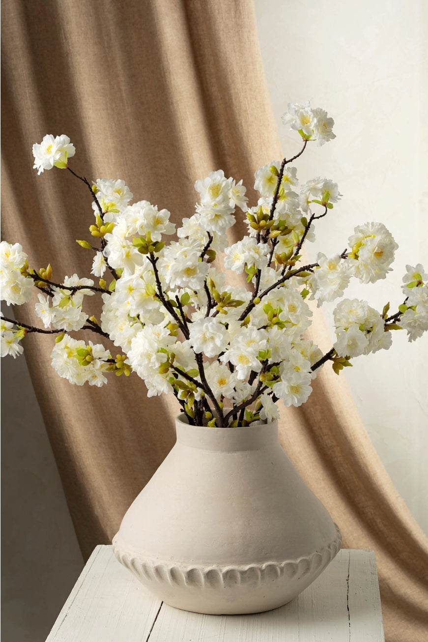 White paper mache vase with white flowers on a wooden surface against a beige curtain background.