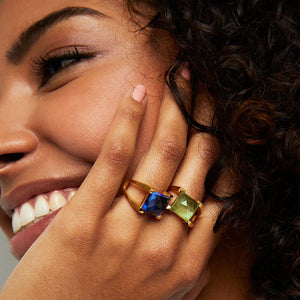 Close-up of a woman's hand wearing multiple mini plaza gold rings featuring blue and green gemstones. Dean Davidson jewelry.