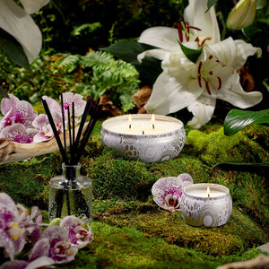 Mokara Orchid candle collection and diffuser with orchid flowers on a mossy surface. Voluspa. 