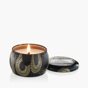 4 ounce tin candle of Voluspa Moso Bamboo with flame lit. 