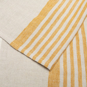 Close-up of linen and cotton fabric towel with yellow and tan stripes on a beige background. Caravan Collection. 