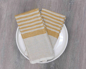 Two mustard striped tea towels on a white plate with a wooden surface background. 