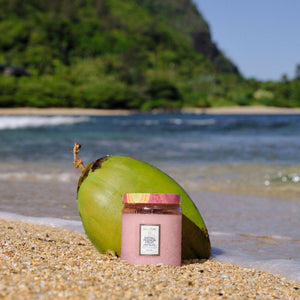 Pink jar with a label on a beach with a coconut and ocean view