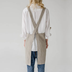 Person wearing a beige linen apron over a white shirt and blue jeans on a plain background