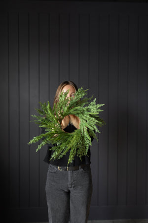 Person holding a large green wreath against a dark wooden panel background