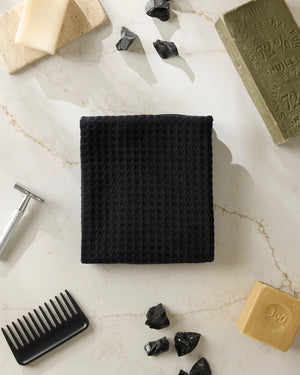 Black waffle-textured washcloth on a marble surface with soap bars and a comb.