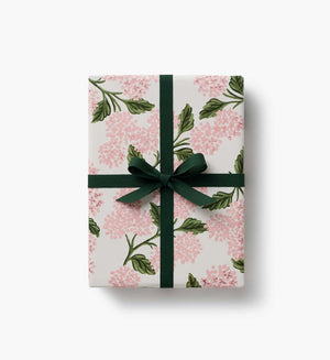 Gift box wrapped in pink floral hydrangea paper and green velvet ribbon finishing bow on a white background. 