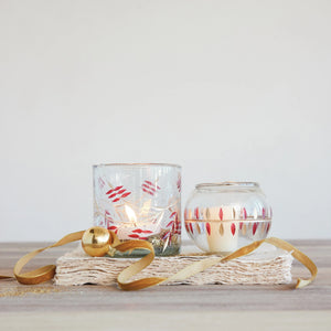 seeded glass candle votive with red and gold painted leaf design on top of book with gold velvet ribbon decor. 