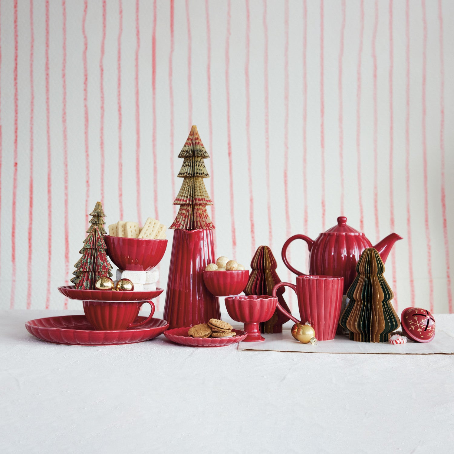 Red ceramic ribbed tableware set with decorative holiday trees against a striped background