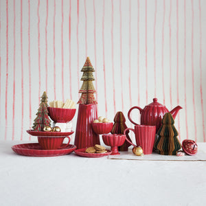 Red ceramic ribbed tableware set with decorative holiday trees against a striped background