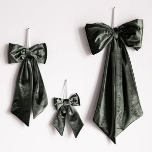 Three dark green velvet bow decorations of different sizes hanging on a plain white wall.