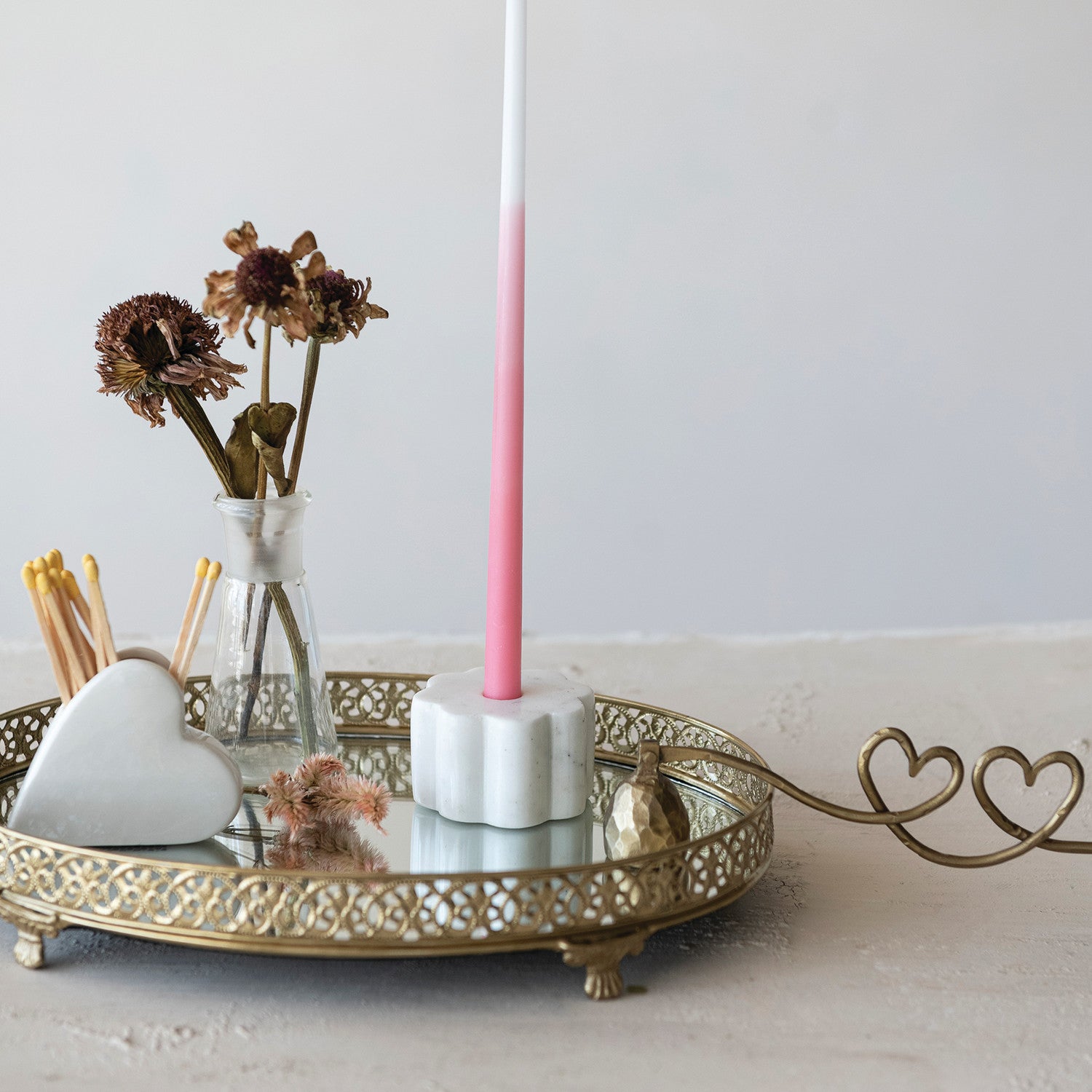 scalloped white marble taper holder with pink candle displayed on gold metal tray. 
