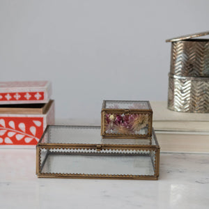 Decorative brass and glass boxes with scalloped edges on a marble surface with a neutral background. 