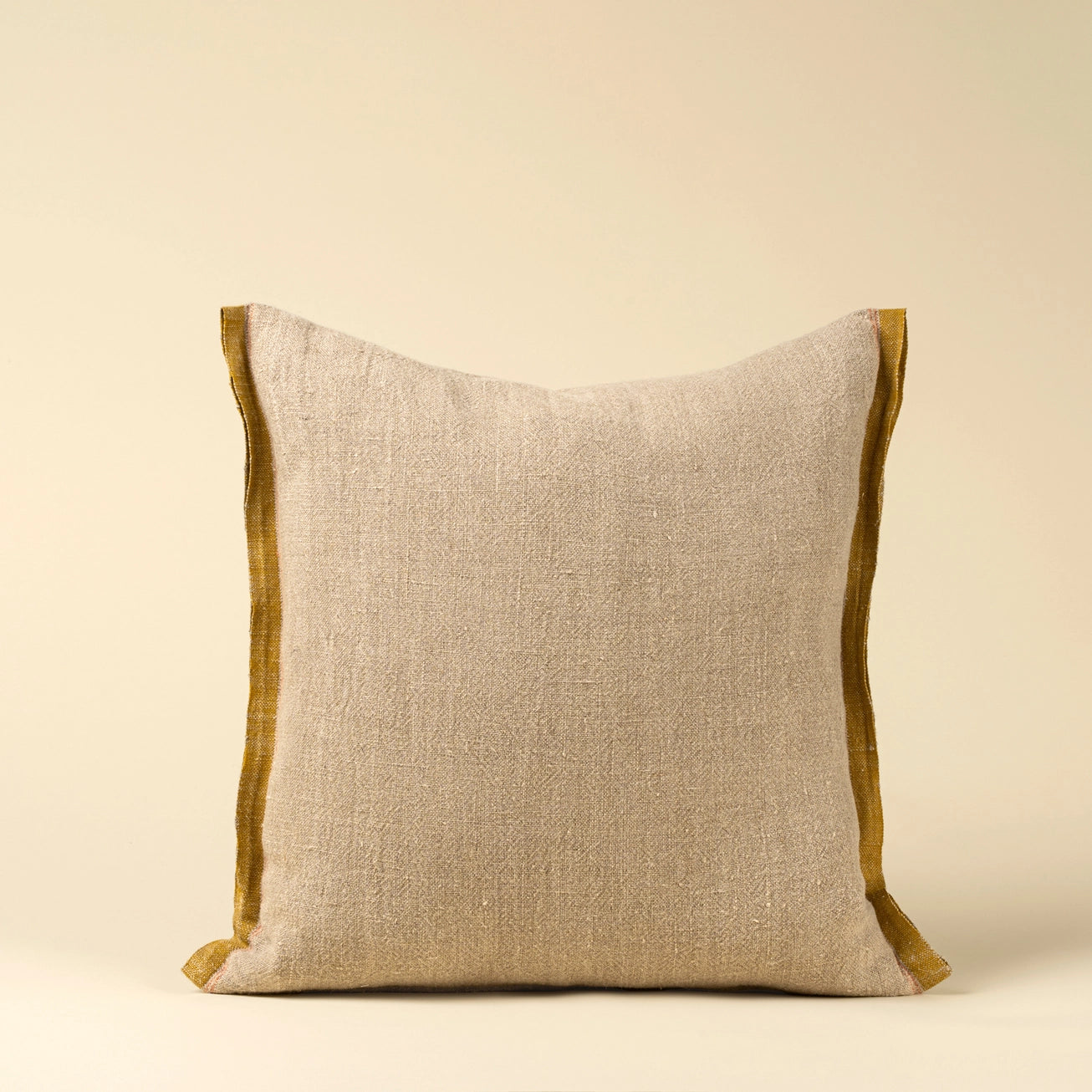 Beige belgian linen pillow with sunflower yellow selvage trim on a beige background. 