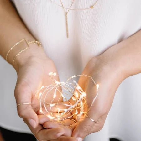 Two hands holding a string of small lights against a white background