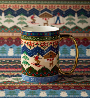 A ceramic mug with a colorful winter ski-themed pattern and a gold handle, set against a matching patterned fabric background.