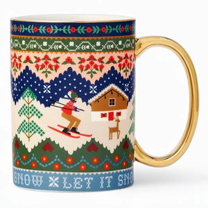 A ceramic mug with a festive winter holiday design featuring a skier, a cabin, trees, and a reindeer, with a gold-colored handle on a white background.