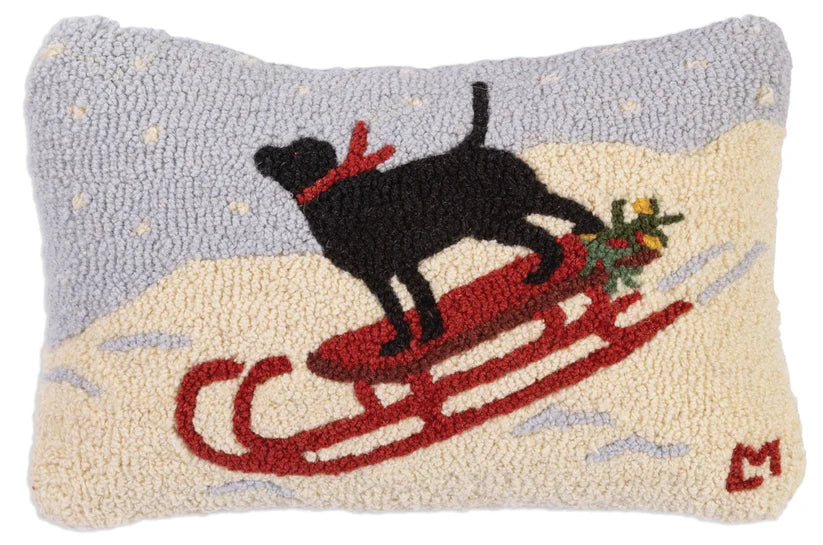 12x18  decorative pillow featuring a black dog on a red sled in a snowy winter scene, with a light blue-gray sky and cream-colored snow. Chandler 4 Corner