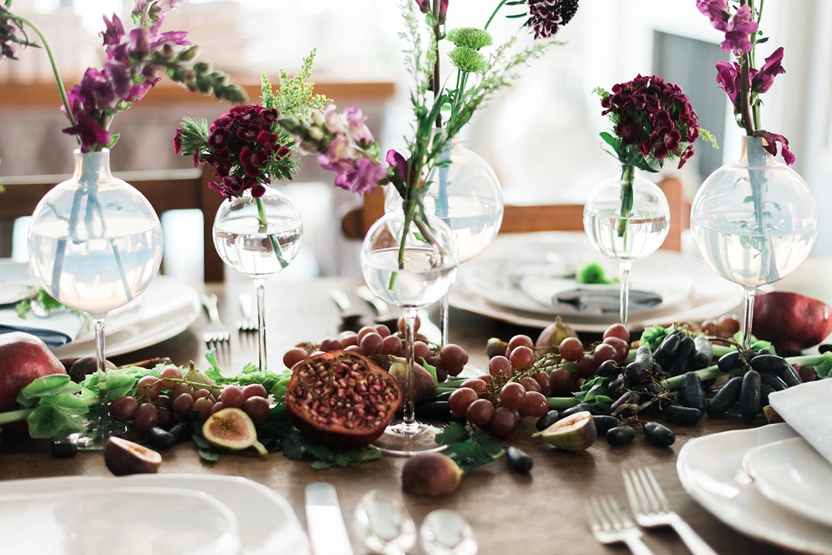 Collection of varying sized glass sphere vases displayed on a rustic burgundy centerpiece display. 
