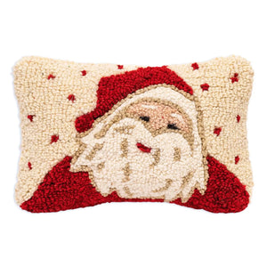 A rectangular hand-hooked Christmas pillow featuring a stylized Santa Claus face and beard in red and cream, with small red snowflake accents on a cream background.