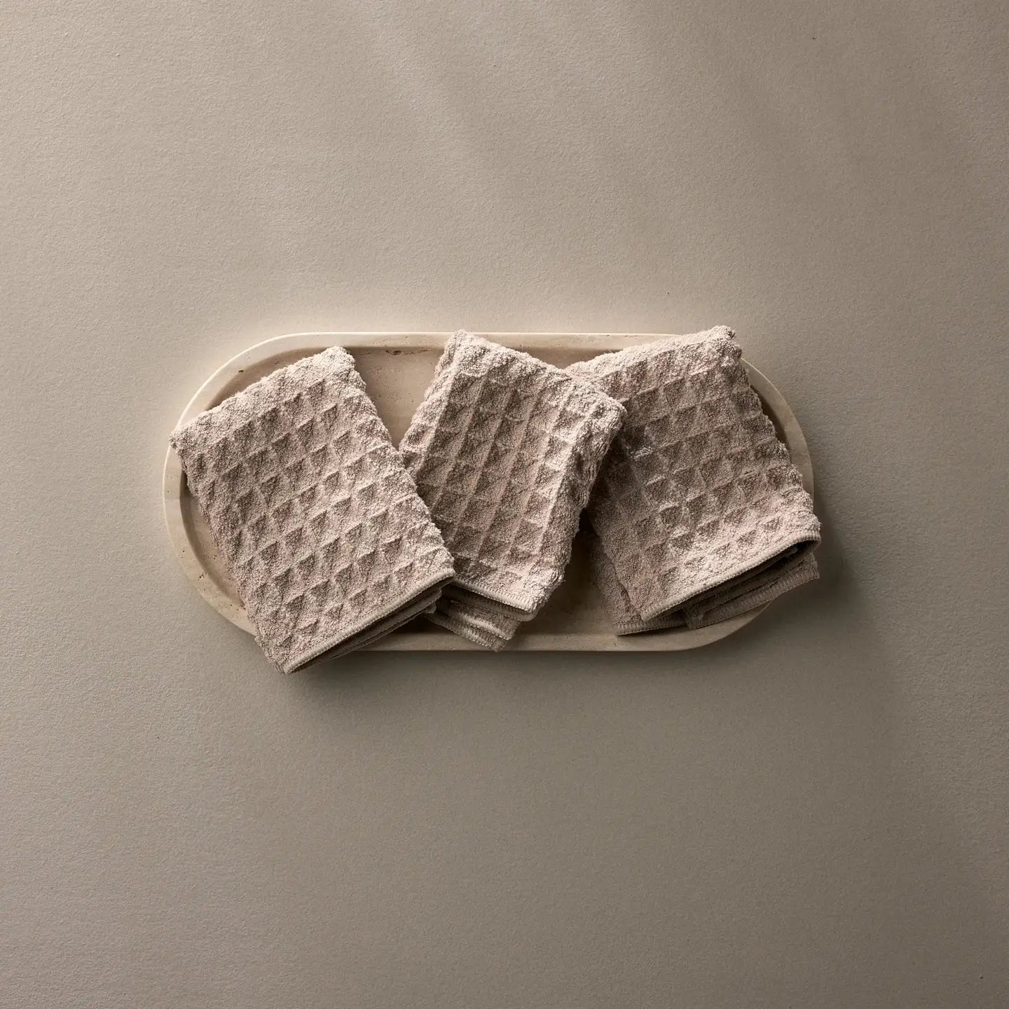 Three folded beige washcloths on a white plate against a beige background