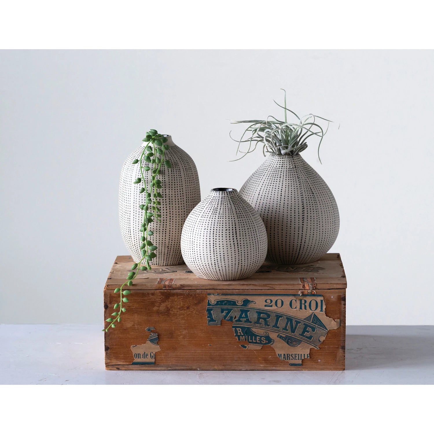 coordinating set of 3 neutral tone textured stoneware vases. Filled with faux stems on top of a rustic box.