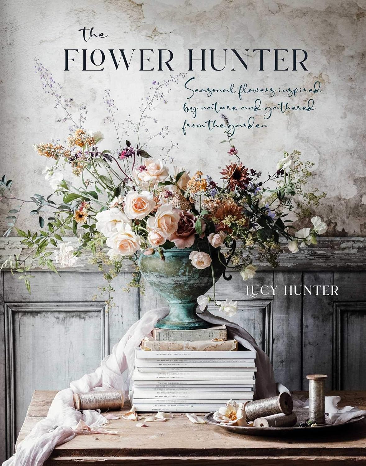 Front cover of "The Flower Hunter" by Lucy Hunter. Seasonal floral arrangement displayed on top of stack of vintage books. 
