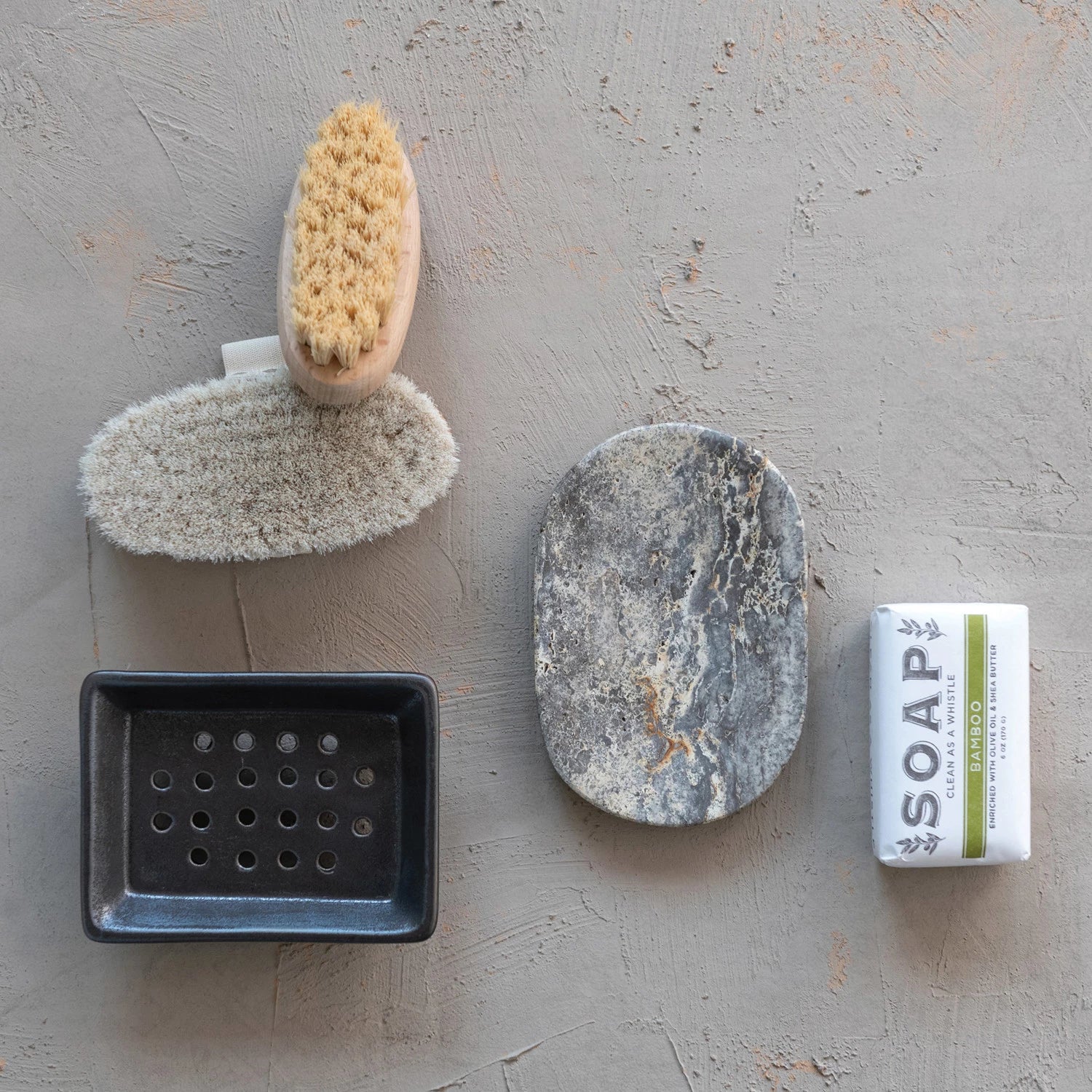 oval travertine soap dish next to bath brushes, bars of soap, and sponge trays.