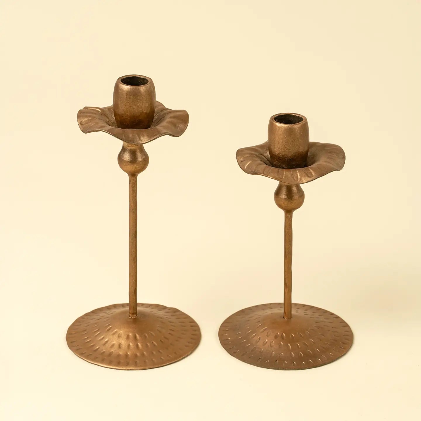Two tulip-shaped brass candle holders on a beige background