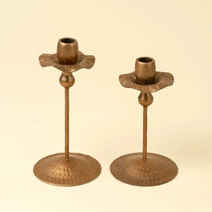Two tulip-shaped brass candle holders on a beige background