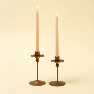 Two tulip-shaped brass candle holders with lit candles on a beige background