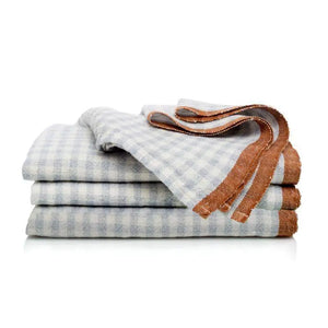Stack of folded blue gingham printed linen napkins with a brown border on a white background. Comes as a set of four. 