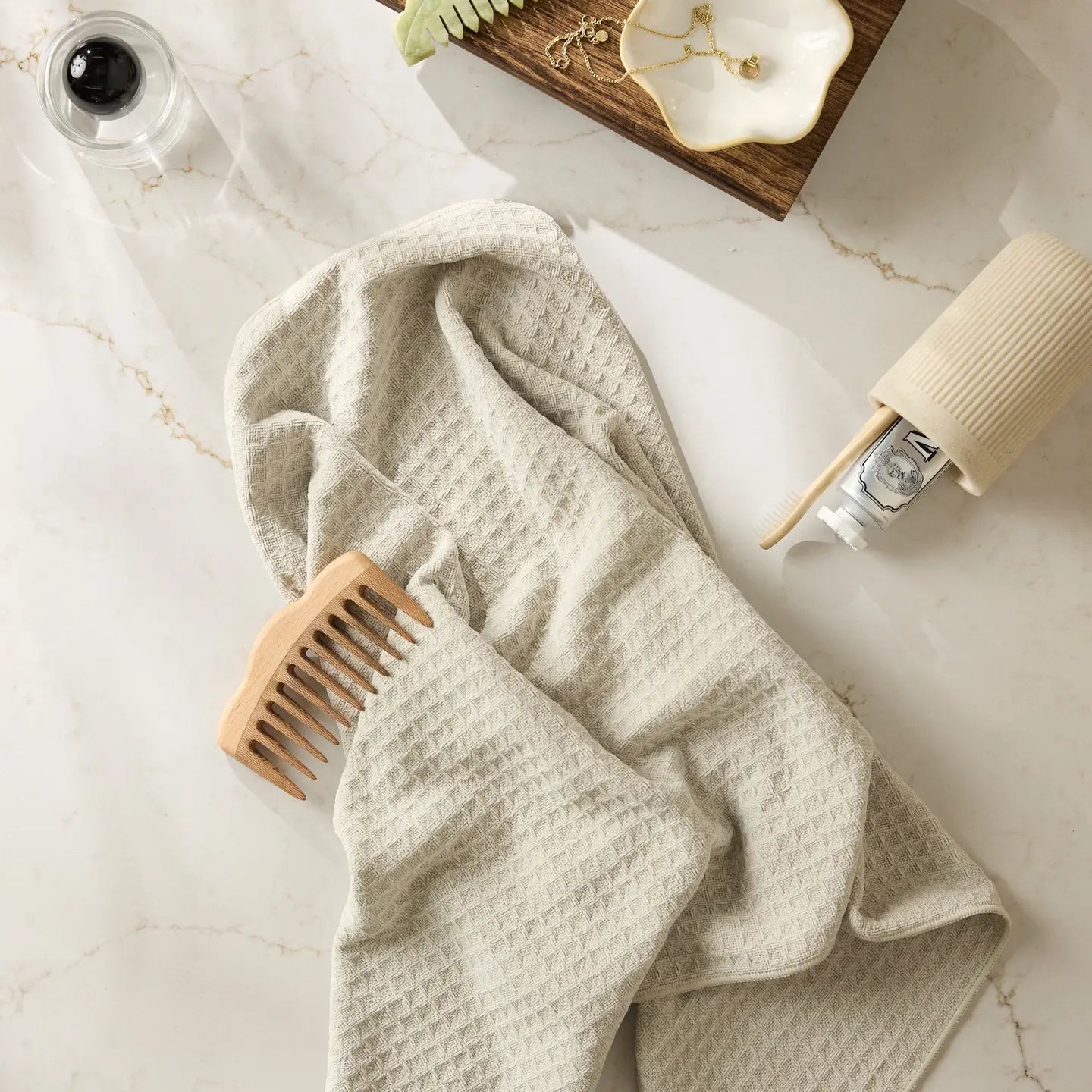 Cream tea towel draped over a wooden comb on a marble surface with skincare products.