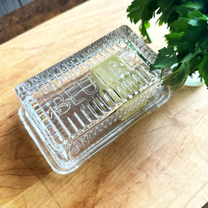 Glass french style butter dish with French word "Beurre" engraved in the lid, displayed on kitchen counter. 