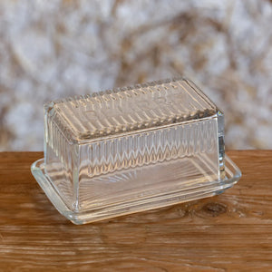 Clear French style glass butter dish with textured lid on a wooden surface. "Beurre" engraved on the top of the lid. 